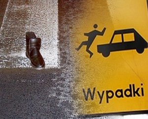 Grafika - z lewej strony na przejściu dla pieszych leży but, z prawej strony znak – piktogram człowiek potrącony przez auto. Pod znakiem napis wypadki