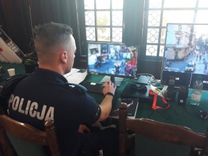 Na zdjęciu widać policjanta patrzącego w monitory z kamer monitoringu