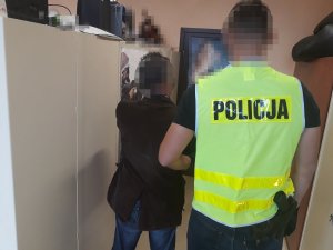 Na zdjęciu widać policjanta prowadzącego zatrzymanego mężczyznę.