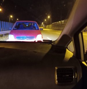 Zdjęcie przedstawia widok z wnętrza policyjnego radiowozu. Przed radiowozem, na autostradzie, stoi zaparkowany samochód osobowy.