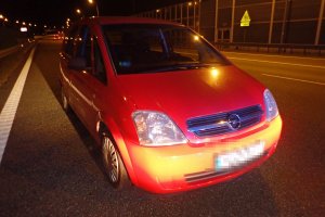 Na zdjęciu widać samochód zaparkowany pod prąd, na lewym pasie autostrady. W tle zdjęcia widać samochody jadące w przeciwnym kierunku.