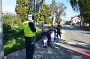 policjant stoi na chodniku i rozmawia z grupą przedszkolaków