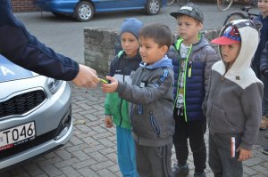 Czterech chłopców stoi przy policyjnym radiowozie. Jeden z nich dostaje od policjanta odblask.