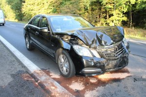 Na zdjęciu widać mercedesa, który ma zgniecioną przednią maskę. Samochód stoi na drodze.