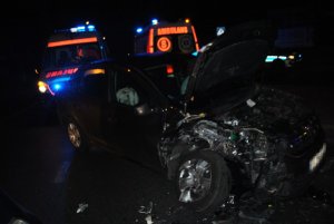 Na zdjęciu widać uszkodzony samochód marki Dacia biorący udział w zdarzeniu. Auto ma podniesioną do góry maskę i urwane przednie koło. W tle zdjęcia widać karetki pogotowia.
