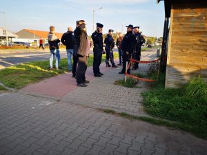Grupa policjantów wraz z dowódcą zabezpieczenia stoi na chodniku przy stadionie