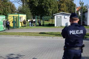 Policjant obserwuje kibiców, którzy kupują bilety w kasie stadionowej