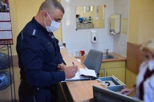 Policjant stoi przy biurku i wypełnia dokumenty