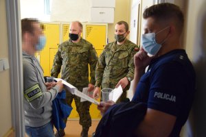 Na korytarzu szpitala stoją policjanci i żołnierze