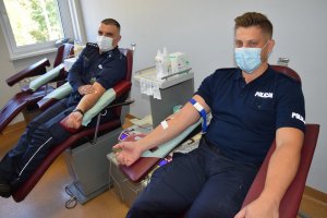 Dwóch policjantów siedzi na fotelach i oddają krew.