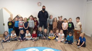 Klasa szkolna. Pod ścianą stoi grupa dzieci oraz policjant