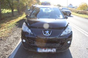 Na zdjęciu widać samochód osobowy, który ma uszkodzony przód. Za samochodem widać karetkę pogotowia