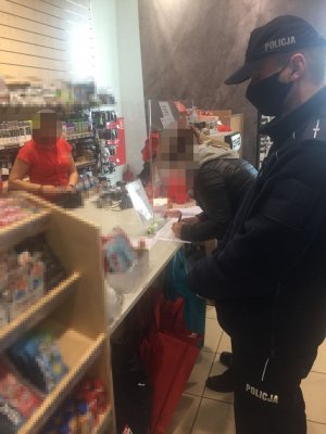 Na zdjęciu widać policjanta, który w sklepie sprawdza przestrzeganie zasad reżimu sanitarnego