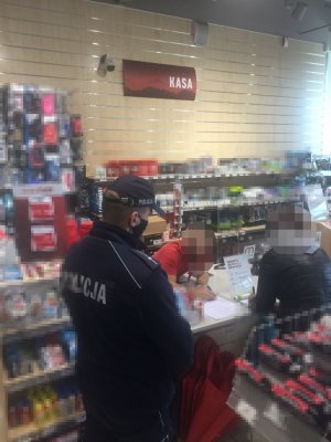 Na zdjęciu widać policjanta, który w sklepie sprawdza przestrzeganie zasad reżimu sanitarnego