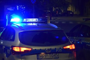 Policyjny radiowóz z włączonymi sygnałami świetlnymi, przed którym stoją policjanci z drogówki