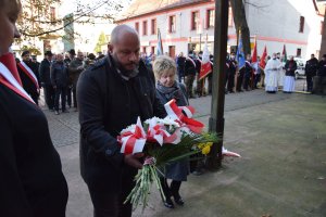 Przedstawiciele Rodziny Katyńskiej stoją z wiązankami kwiatów przed tablicami pamięci