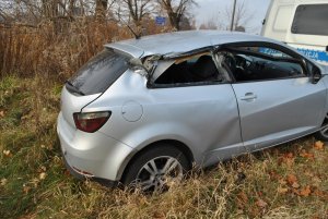 Na zdjęciu widać samochód osobowy w przydrożnym rowie. Auto ma wybite szyby od strony pasażera. W tle zdjęcia widać policyjny radiowóz