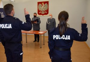 Dwoje policjantów z uniesionymi palcami składają rotę ślubowania. W tle zdjęcia widać szefa i wiceszefa tarnogórskich policjantów.