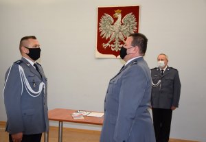 Komendant Powiatowy Policji w Tarnowskich Górach młodszy inspektor Sławomir Bylicki przyjmuje meldunek od Naczelnika Wydziału Prewencji komisarza Piotra Skolika. W tle zdjęcia widać Pierwszego Zastępcę Komendanta Powiatowego Policji w Tarnowskich Górach komisarza Waldemara Czaplę. Na ścianie widać Godło Polski.