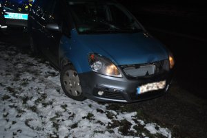 Na zdjęciu widać samochód, który ma uszkodzoną maskę i pękniętą przednią szybę. W tle widać napis &quot;Policja&quot; widniejący na radiowozie