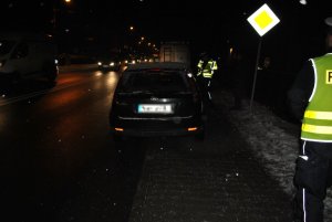 Na poboczu drogi zaparkowany samochód biorący udział w zdarzeniu. Obok pojazdu widoczni dwaj policjanci