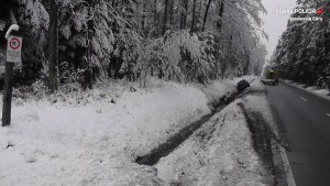 Na środku drogi biegnącej przez las znajduje się laweta. W przydrożnym rowie leży pojazd. Okolica jest cała zaśnieżona.