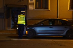 Na zdjęciu widać policjanta, który zatrzymuje do kontroli drogowej kierowcę samochodu.