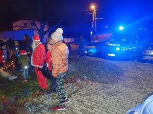 Grupa osób. W tle zdjęcia widać policyjny radiowóz z włączonymi sygnałami świetlnymi.