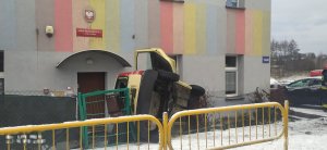 Na zdjęciu widać leżący na boku samochód osobowy. Auto opiera się o elewację budynku.