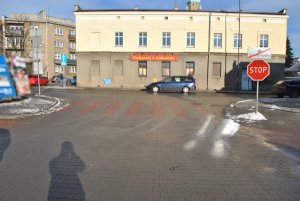 Na zdjęciu widać wyjazd z parkingu sklepowego z widocznym przejściem dla pieszych, przed którym widać znak STOP.