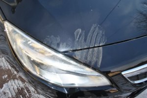 Maska samochodu, na której odbita jest dłoń.