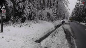 Na środku drogi biegnącej przez las znajduje się laweta. W przydrożnym rowie leży pojazd. Okolica jest cała zaśnieżona.