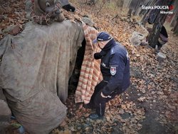 Teren leśny, na którym znajduje się rozbity namiot. Policjant odsłania koc imitujący wejście do namiotu.