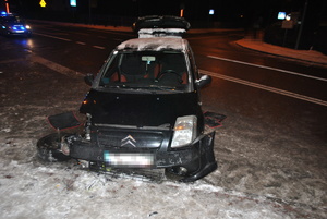 Samochód marki citroen, który ma uszkodzony przód i urwane koło od strony pasażera. W tle widać policyjny radiowóz z włączonymi sygnałami świetlnymi.