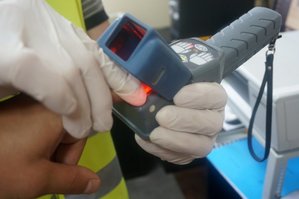 Na fotografii widać dłonie oraz urządzenie do pobierania odcisków linii papilarnych