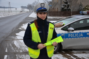 na zdjęciu st. sierż. Anna Szweda z komendy powiatowej policji w Tarnowskich Górach stojąca przy radiowozie, trzymająca w ręku odblaski przekazane przez starostwo powiatowe