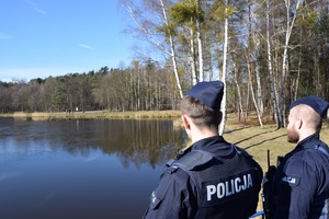 policjanci w niebieskich mundurach obserwują teren nad zbiornikiem wodnym