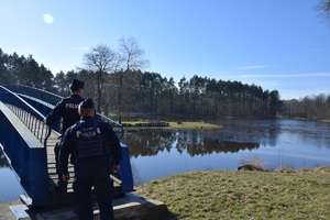 policjanci w niebieskich mundurach obserwują teren nad zbiornikiem wodnym wchodząc na niebieski most