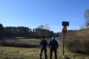 policjanci w niebieskich mundurach obserwują teren nad zbiornikiem wodnym, obok znak zakaz kąpieli