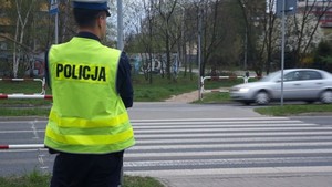 policjant w niebieskim mundurze i kamizelce odblaskowej obserwuje przejście dla pieszych