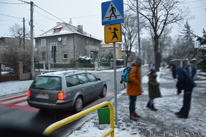 policjant w niebiskim mundurze rozmawia z najmłodszymi uczestnikami ruchu drogowego w rejonie przejścia dla pieszych