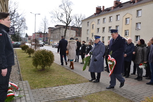 przedstawiciele służb mundurowych, władz miasta i powiatu i mieszkańcy pod pamiątkową tablicą przed budynkiem komendy policji