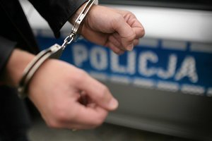 dłonie skute kajdankami, w tle napis policja na niebieskim tle