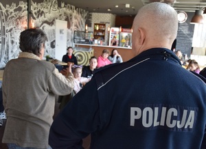 policjant w niebieskim mundurze w trakcie wypowiedzi do obywateli Ukrainy, z lewej strony osoba tłumacząca uczestnikom słowa policjanta