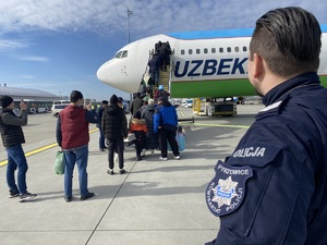 policjant w niebieskim mundurze, na lewym ramieniu naszywka z napisem &quot;Pyrzowice komisariat policji&quot;, obserwuje pasażerów wsiadających do samolotu
