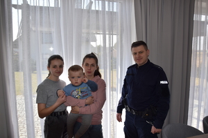 na zdjęciu dzielnicowy w mundurze stojący obok dwóch kobiet, jedna z nich trzyma na ręku dziecko