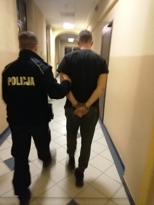 policjant prowadzący korytarzem mężczyznę skutek w kajdanki na ręce z tyłu,