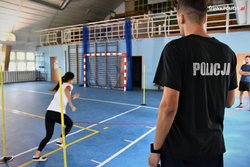 policjant w czarnej koszulce z napisem policji obserwuje kobietę biegnącą na torze przeszkód w sali gimnastycznej