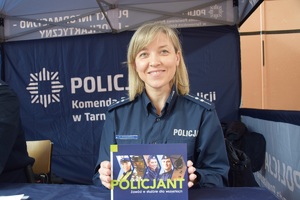 policjantka w niebieskim mundurze przed niebieskim namiotem z plakatem w rękach