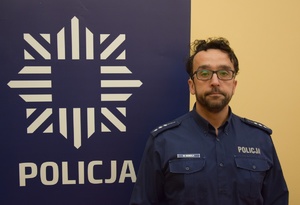 policjant w niebieskim mundurze, obok baner z logiem policji i napisem policja